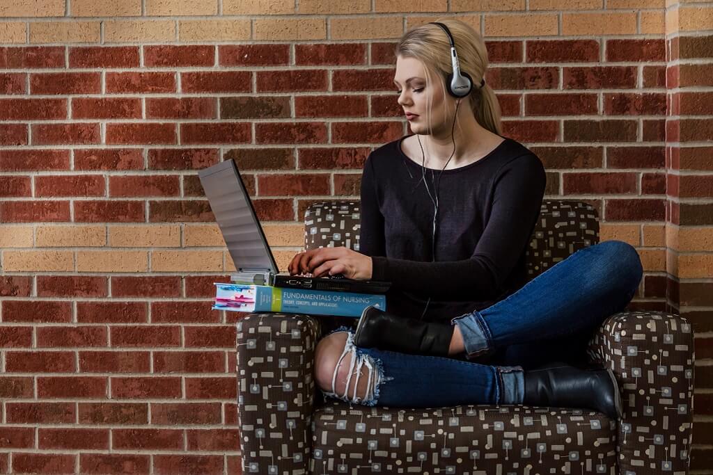 A female sitting on a coach with a laptop. 