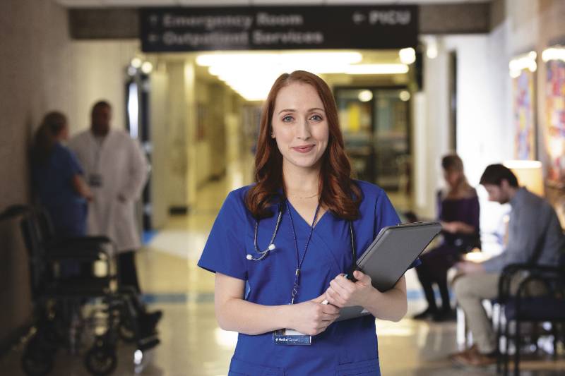 Nurse smiling for photo in hallway of hospital.