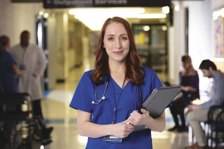 Nurse posing in a healthcare hallway setting.