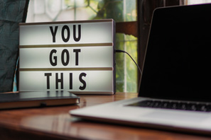 A computer on a desk with some decorative words in the background: You Got This.