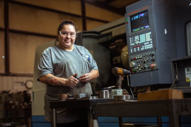 Manid Grubbs poses in front of a CNC machine with a measuring gauge in her hand.