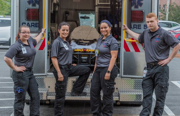 Four paramedic students stand behind an ambulance with open doors.