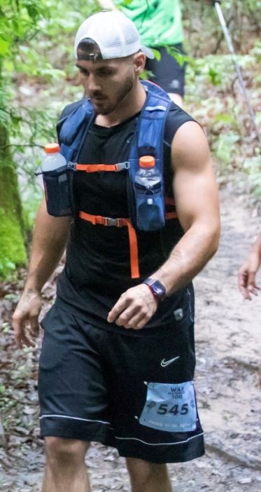 A photo of Frank Robinette hiking in the woods with a backback and water bottles.