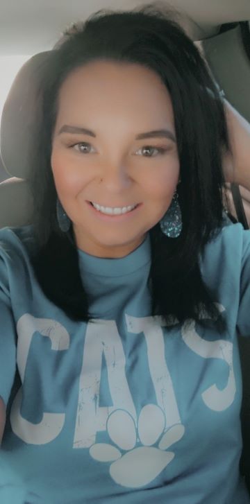 Sarabeth Alcorn takes a selfie while she is in her vehicle. She is wearing a light blue shirt with the word CATS and a paw print on it.