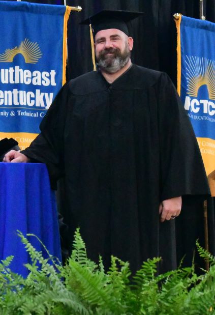 Tom Busic stands on the graduation stage while he is wearing his cap and gown.