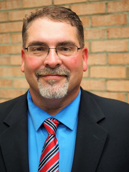 Dr. Vic Adams poses for a photograph in front of a brick wall.