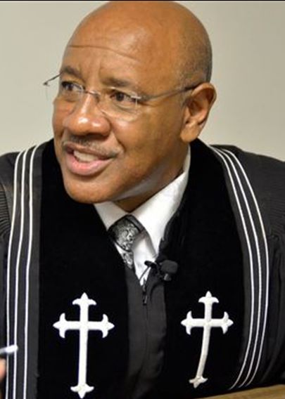 Reverend Ronnie Hampton is preaching when this photo was taken. He is wearing a black robe with white embroidered crosses.