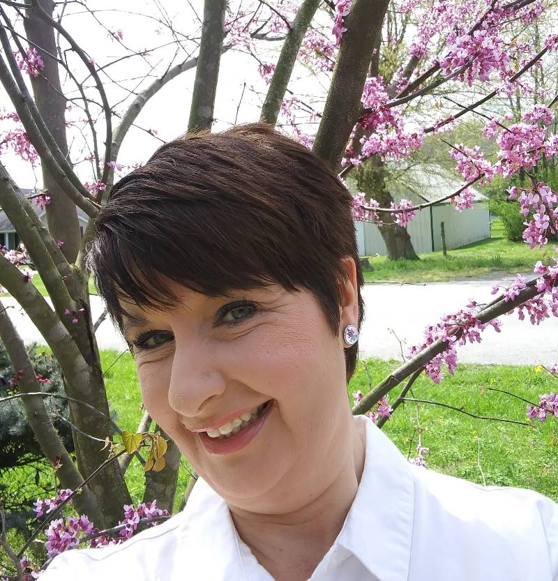 Allie Manning, a female, is smiling and posing in front of a bloomed red bud tree.