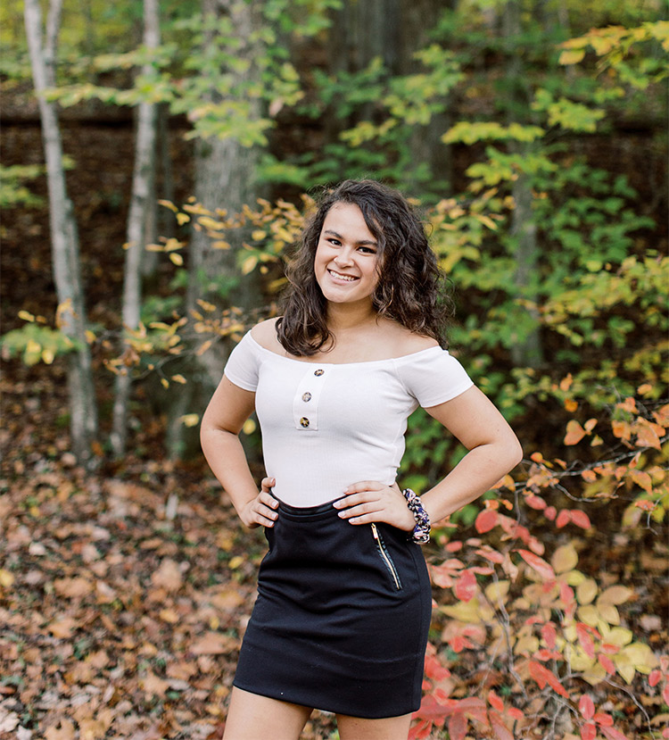 A portrait of Janna Vaught. She is posing outside in the woods.