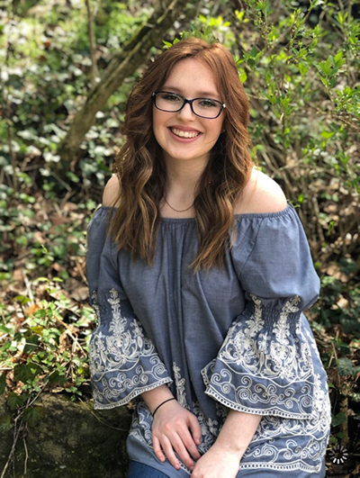 Mady Haynes posting outside in front of some green bushes.