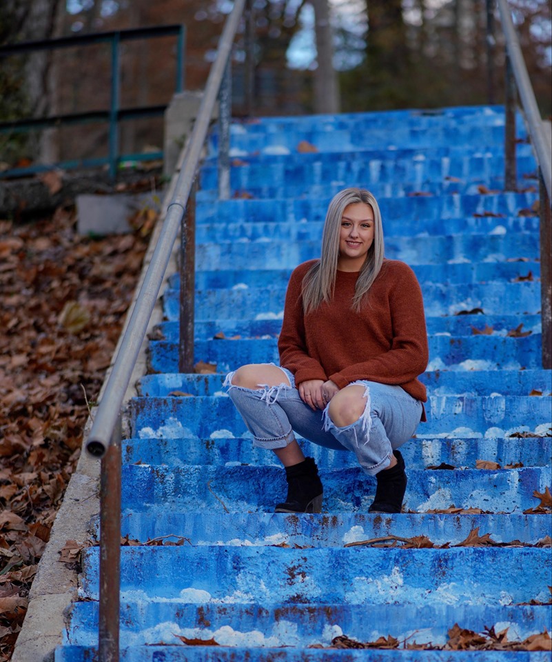 A portriat of Shelby Herrell. She is posing on blue steps.