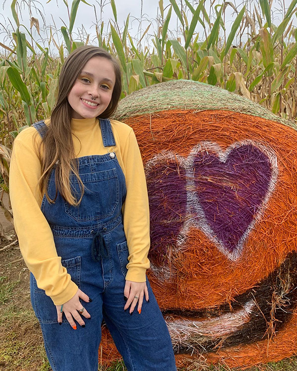 Sheyanna Gladson earned the student of the month award for March. She is smiling outside next to a roll of hay or straw.